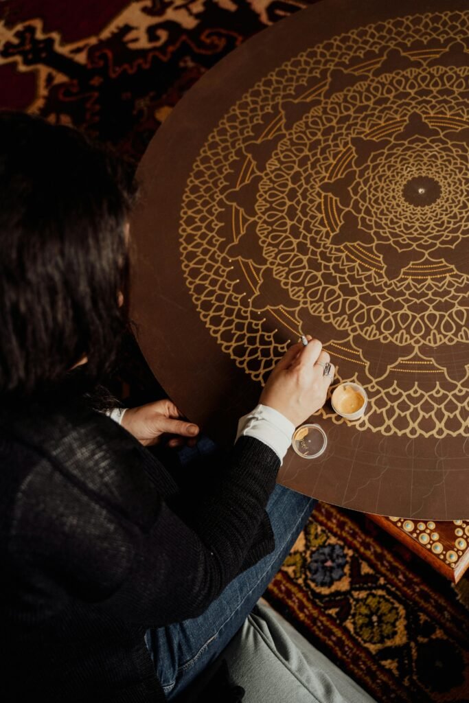 Woman intricately painting a geometric mandala pattern on a table indoors. Creative process.